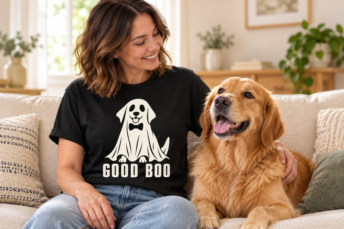 Woman on a sofa wearing the black Good Boo ghost dog tee next to her golden retriever